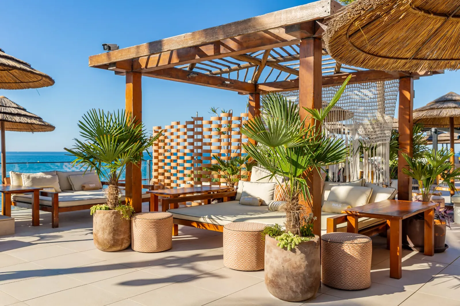 Zona lounge bajo pérgola de madera con palmeras en macetas en Max Beach